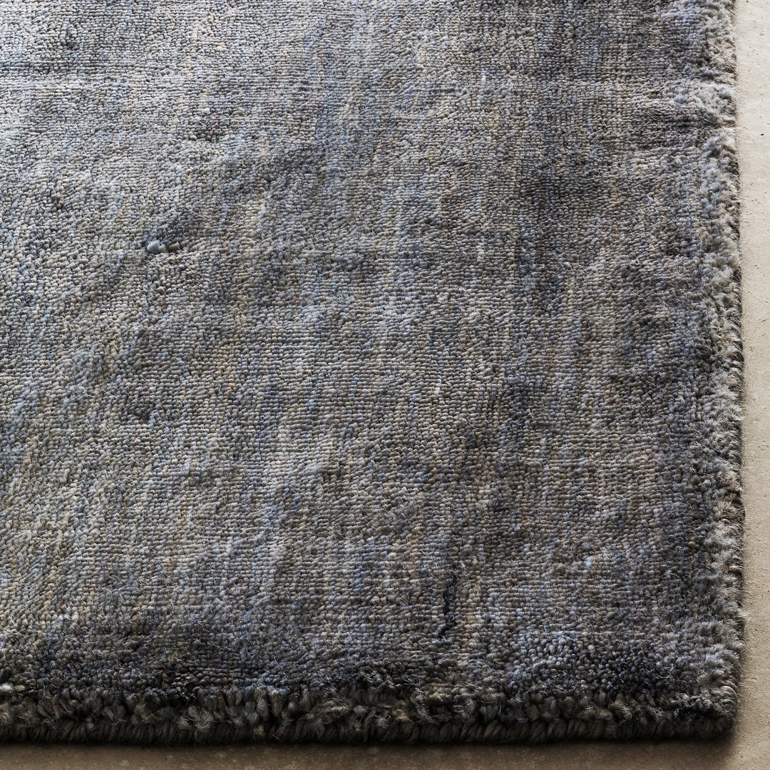 Textured area rug in shades of gray with subtle blue and silver accents, featuring a modern, abstract pattern.
