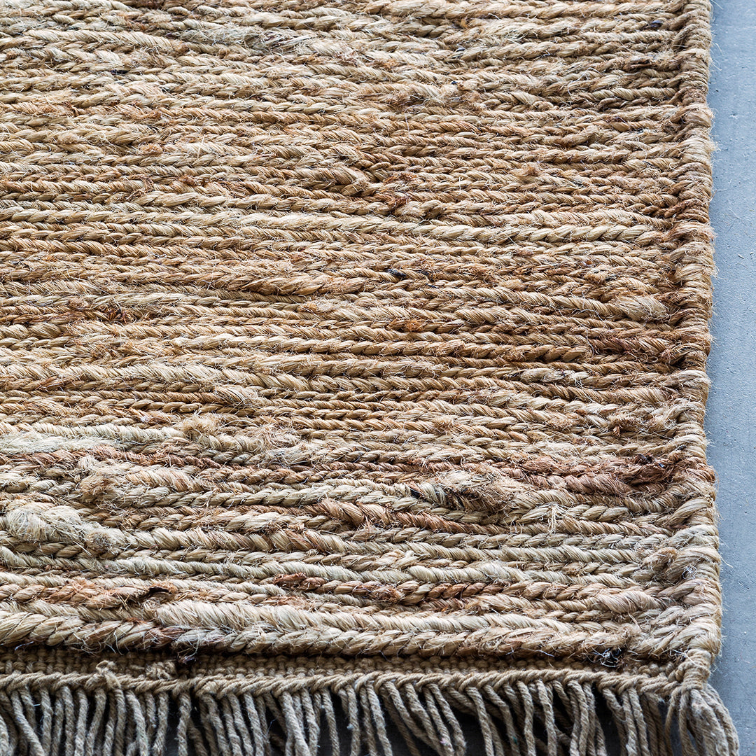 Textured beige and tan woven rug with subtle patterns and fringed edges, ideal for cozy home decor.