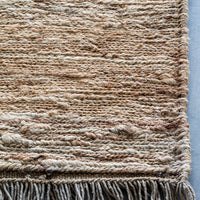 Textured beige and tan woven rug with subtle patterns and fringed edges, ideal for cozy home decor.