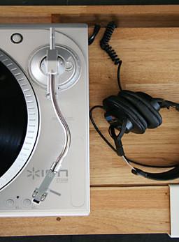 Silver turntable with a black vinyl record and black headphones on a wooden surface. Simple, sleek design and modern colors.