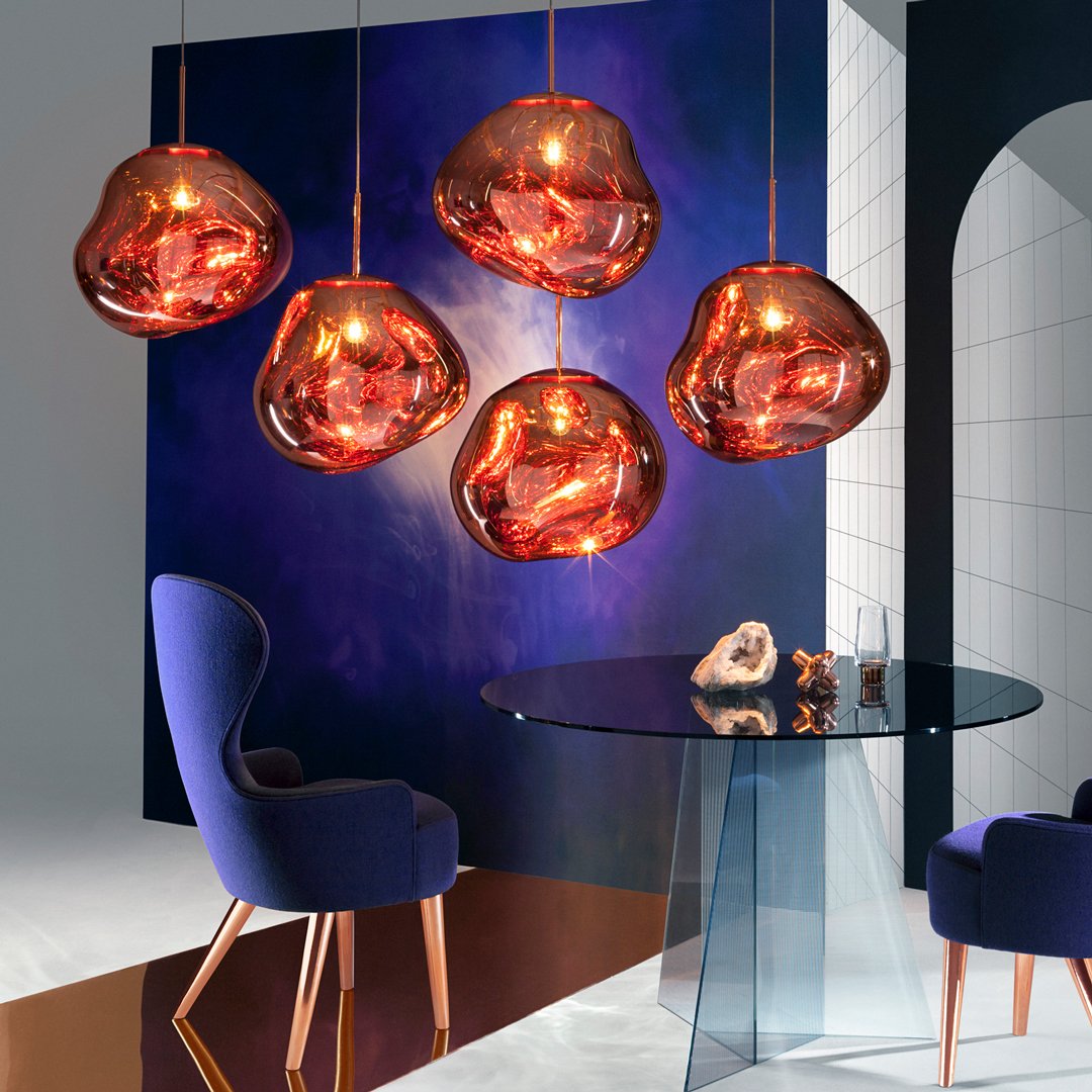 Stylish copper pendant lights against a deep blue wall, paired with a sleek glass table and rich purple chair.