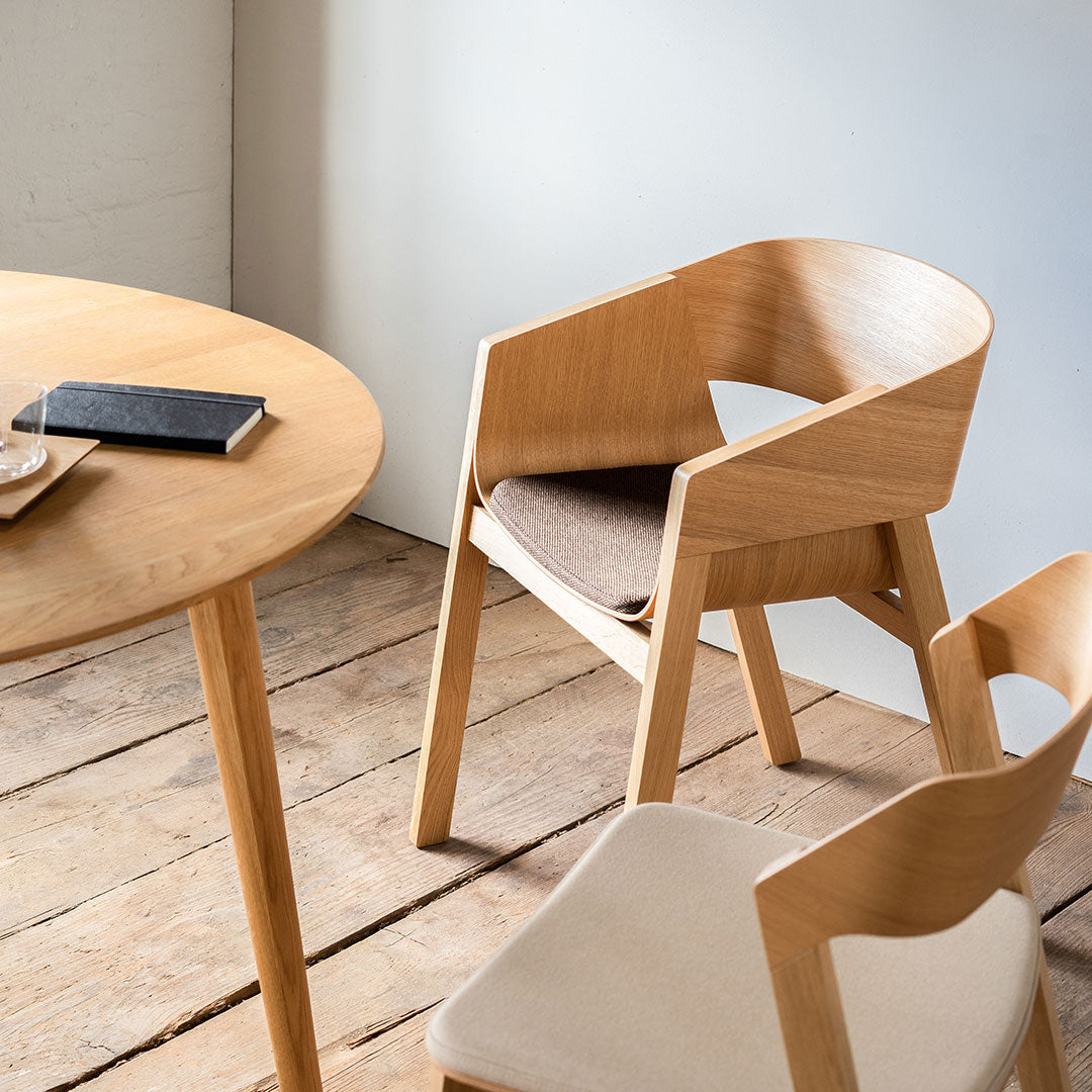 Light natural wood chair with a textured beige seat, paired with a round wooden table on rustic floorboards.