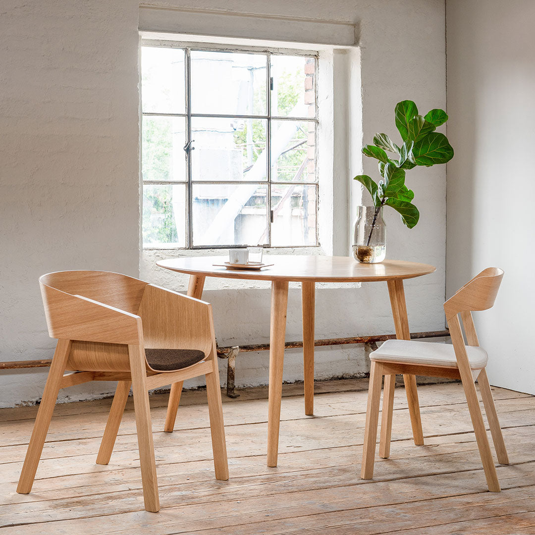 Light wood dining set featuring a round table with a natural finish and beige upholstered chairs, enhancing a minimalist aesthetic.