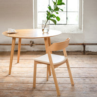 Light wood round table with natural finish and modern white chair, complemented by minimalistic decor.