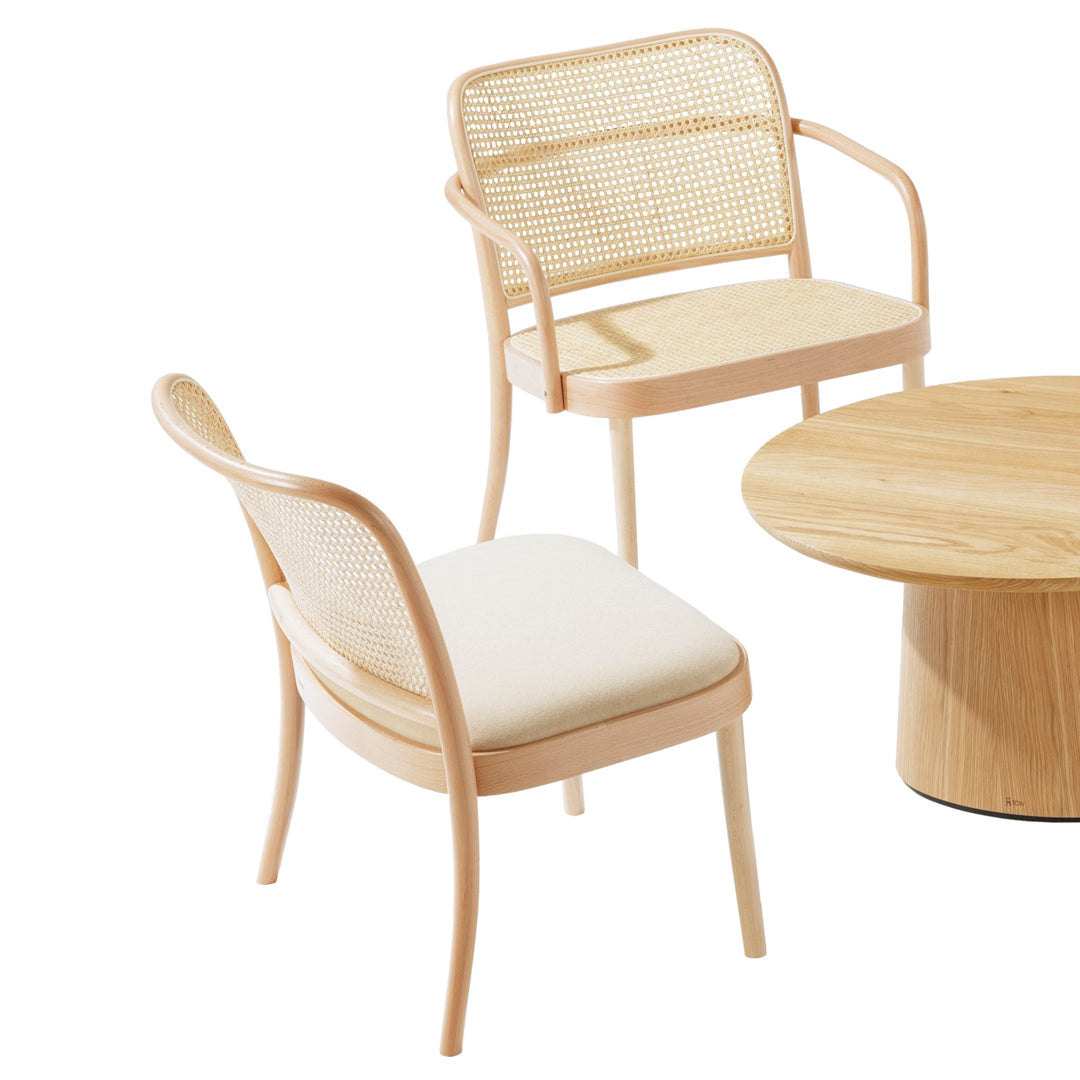 "Light wooden chairs with woven backs and cream cushions, paired with a round wooden table, featuring natural tones."