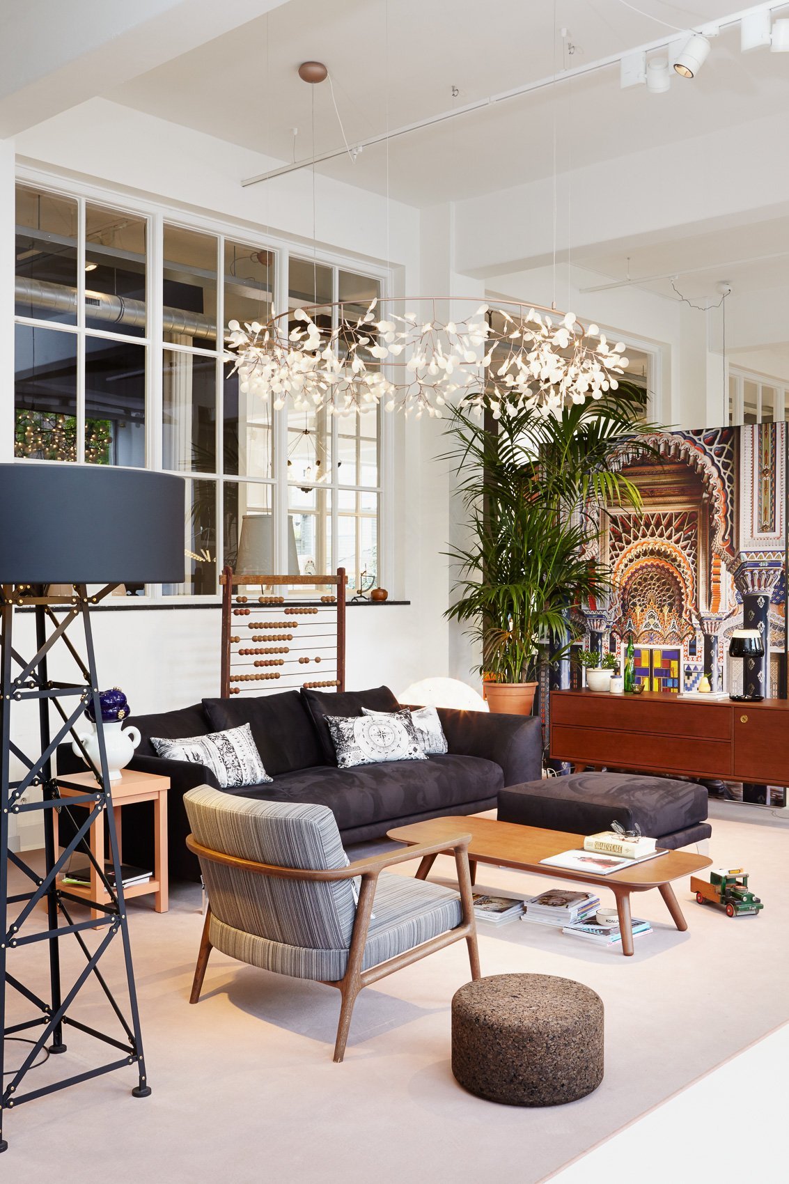Modern living room featuring charcoal gray sofas, patterned cushions, wood accents, and a variety of greenery.