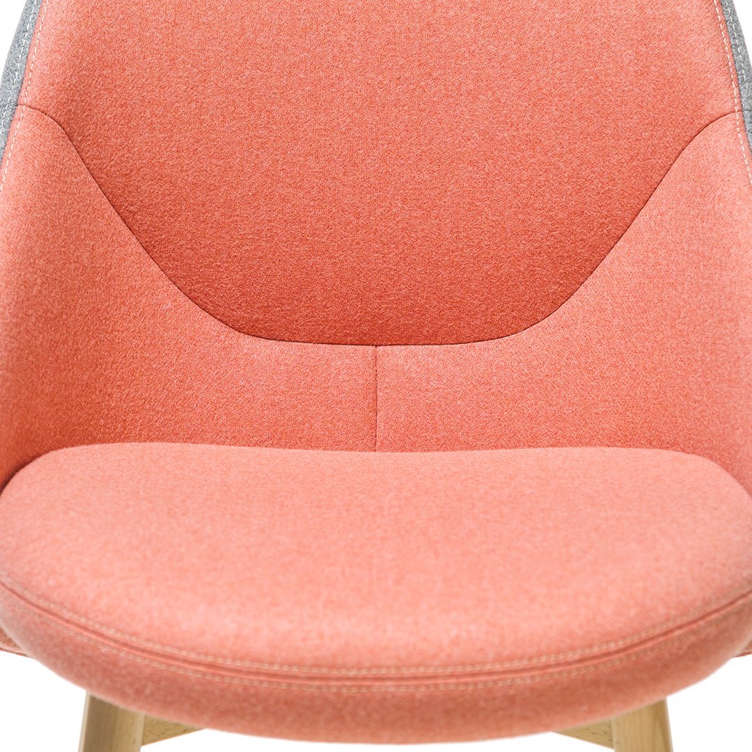 Coral pink fabric chair with a smooth texture and minimalist design, featuring light wood accents.