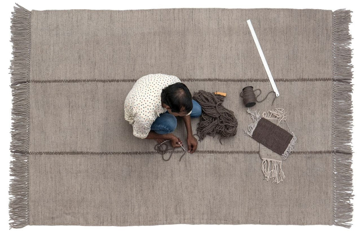 Gray woven rug with subtle stripes and fringed edges, showcasing a minimalist pattern. Perfect for modern decor.