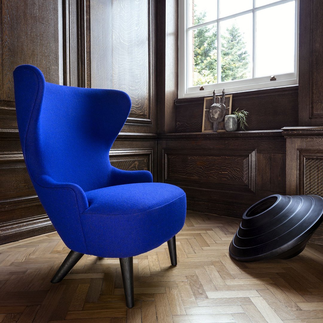 Vibrant blue upholstered chair with sleek black legs, set against a warm wood-patterned floor.