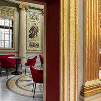 Elegant red chairs against a backdrop of ornate gold detailing and patterned marble flooring.