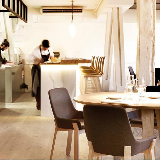 Modern dining space with light wood tones, dark gray chairs, and minimalist decor featuring warm lighting.