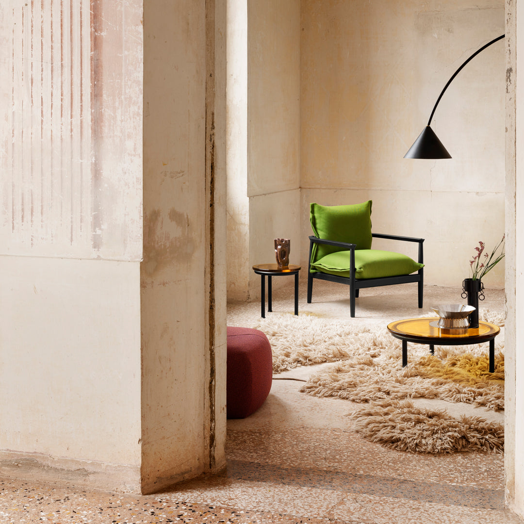Modern living room with a vibrant green chair, soft beige rug, and dark accents in a neutral-toned space.