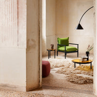 Modern green chair, black lamp, round yellow and black tables, and soft beige rug in a minimalist interior.