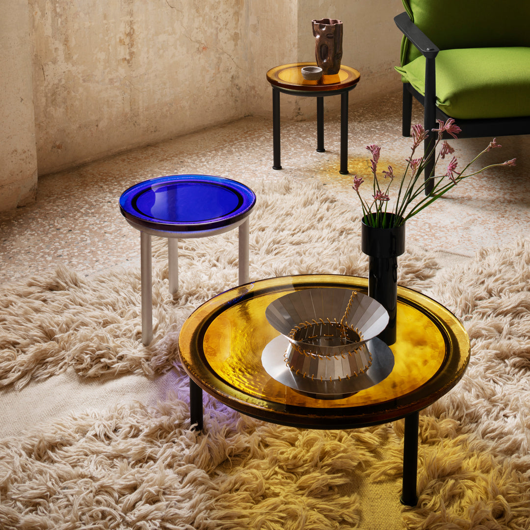 "Colorful side tables with amber and blue patterns, set on a textured cream carpet and surrounded by modern decor."