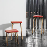 Modern stools with a soft red seat and natural wood legs, set against a sleek, minimalist background.