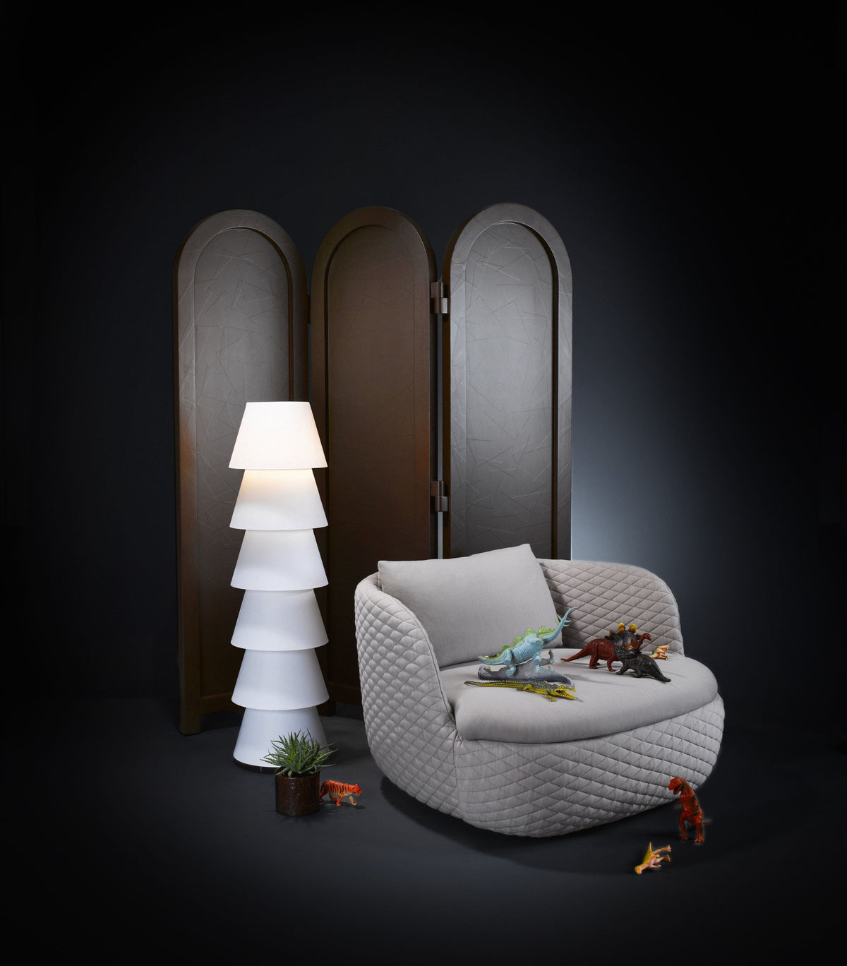 Cozy gray armchair with woven texture, paired with a white tiered lamp and dark wooden screen. Bright accent colors from toys.