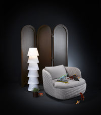 Cozy gray armchair with woven texture, paired with a white tiered lamp and dark wooden screen. Bright accent colors from toys.