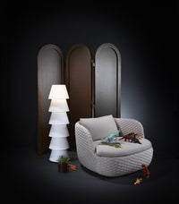 Stylish gray armchair with quilted pattern, surrounded by a white lamp and dark wooden screen, set against a black background.