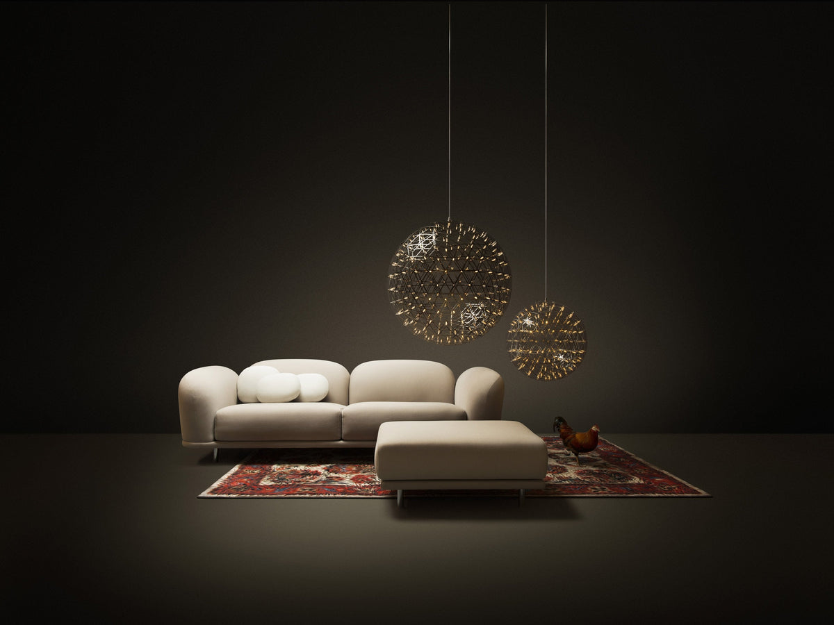 Beige sofa with a plush ottoman on a red patterned rug, showcased in a dark, minimalistic setting.