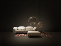 Beige sofa with a plush ottoman on a red patterned rug, showcased in a dark, minimalistic setting.