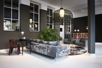 Stylish gray velvet sofa and burgundy chair with geometric patterns, set against dark walls and a bright floor.