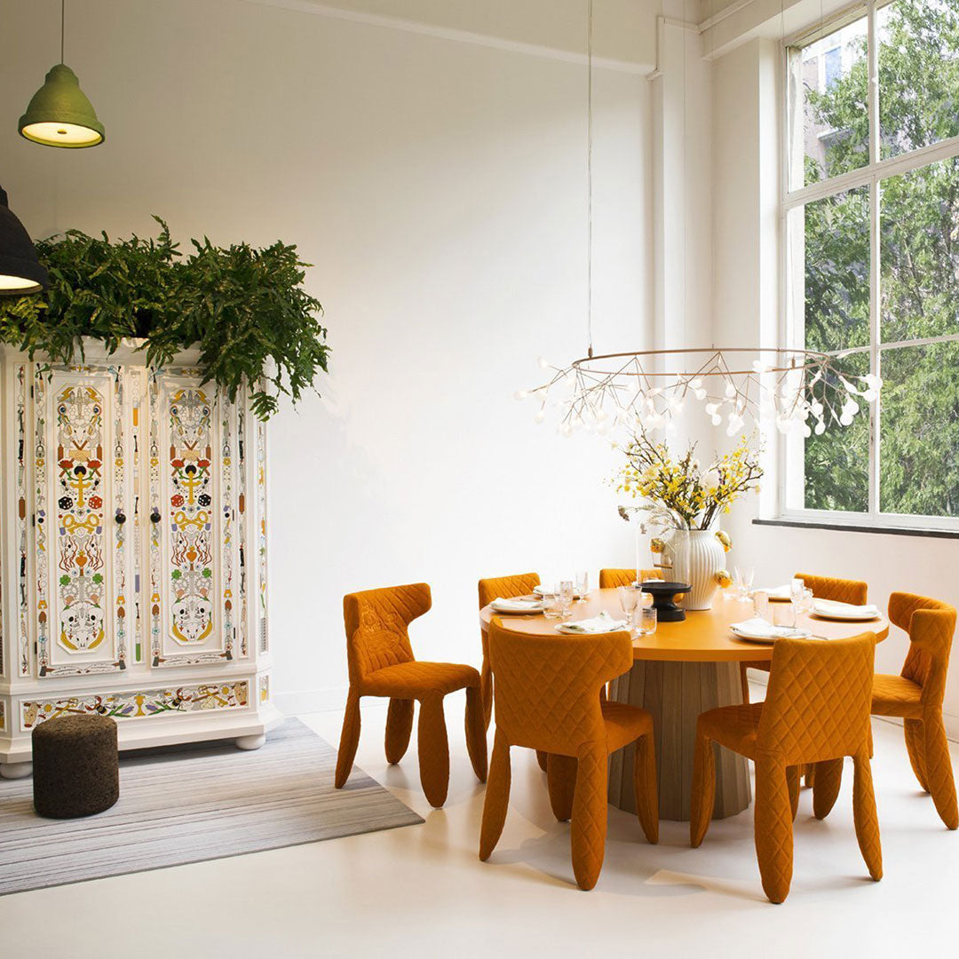 Colorful dining set featuring vibrant orange chairs and a floral patterned cabinet against a bright, minimalistic backdrop.