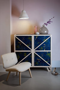 Modern sideboard with blue abstract patterns and white frame, paired with a neutral-colored chair and soft pastel backdrop.