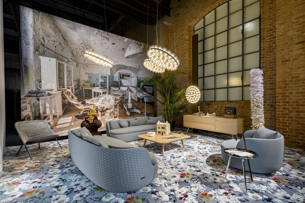 Gray modern sofas on a colorful floral rug, with warm wood tones and a striking backdrop of exposed brick and bright lighting.