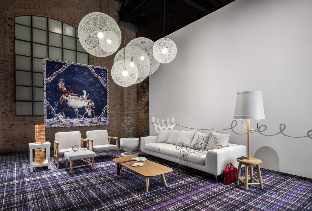 Modern lounge with a purple plaid rug, white furniture, and colorful wall art; bright pendant lights enhance the decor.