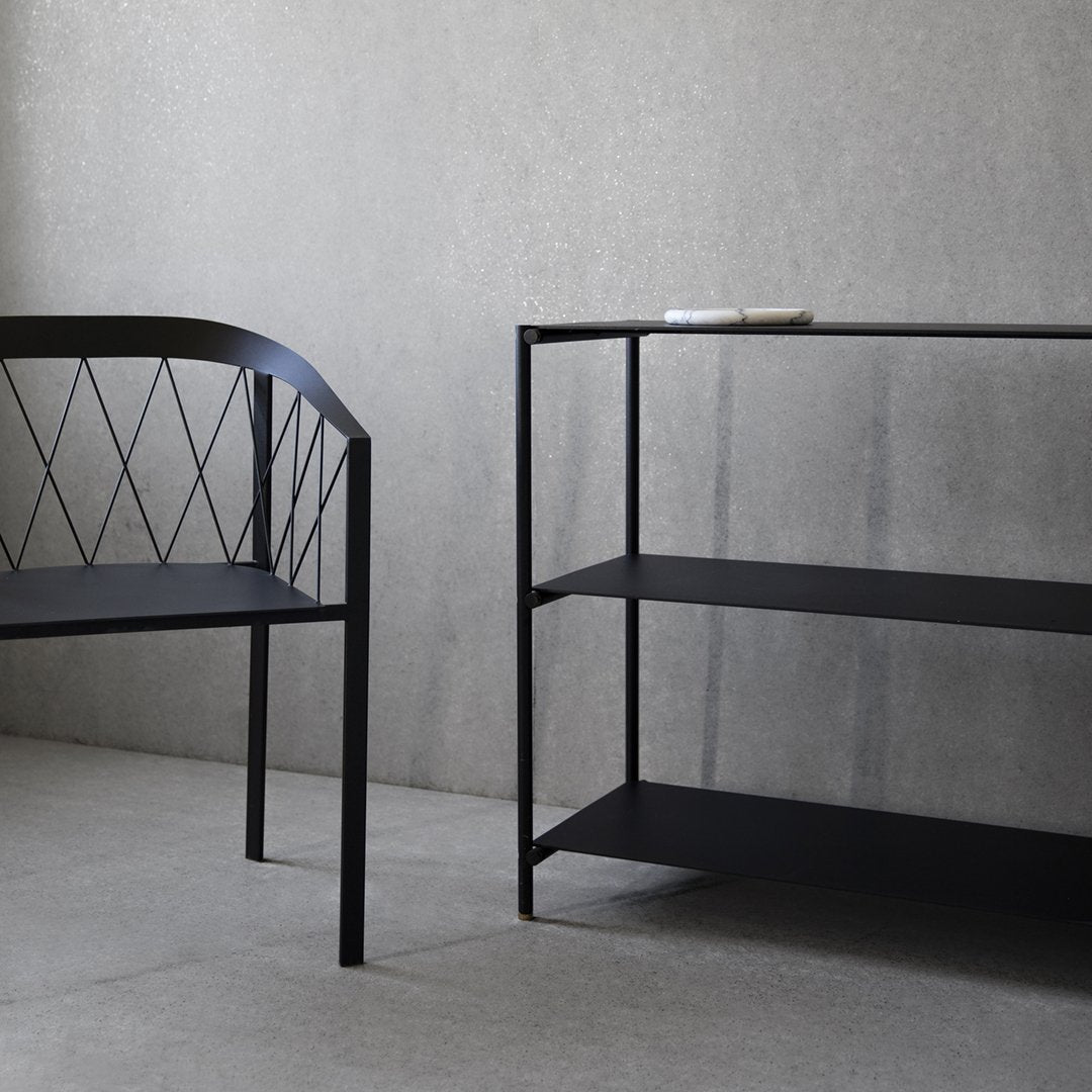 Black metal bench with diamond pattern and matching shelf against a smooth gray wall, featuring minimalist design.