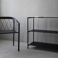 Black metal bench with diamond pattern and matching shelf against a smooth gray wall, featuring minimalist design.