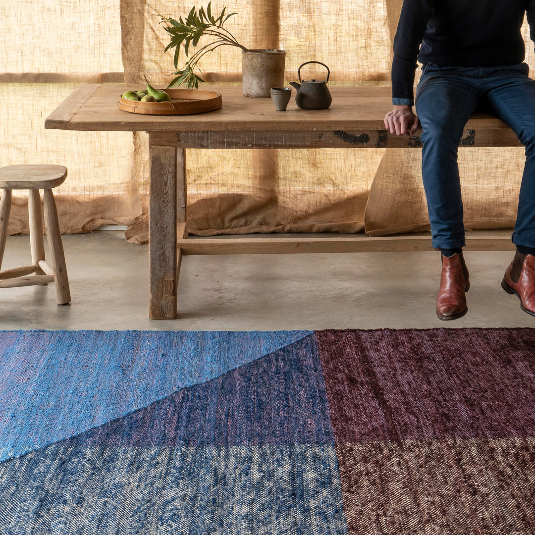 Colorful geometric area rug featuring shades of blue, maroon, and gray patterns on a textured surface.