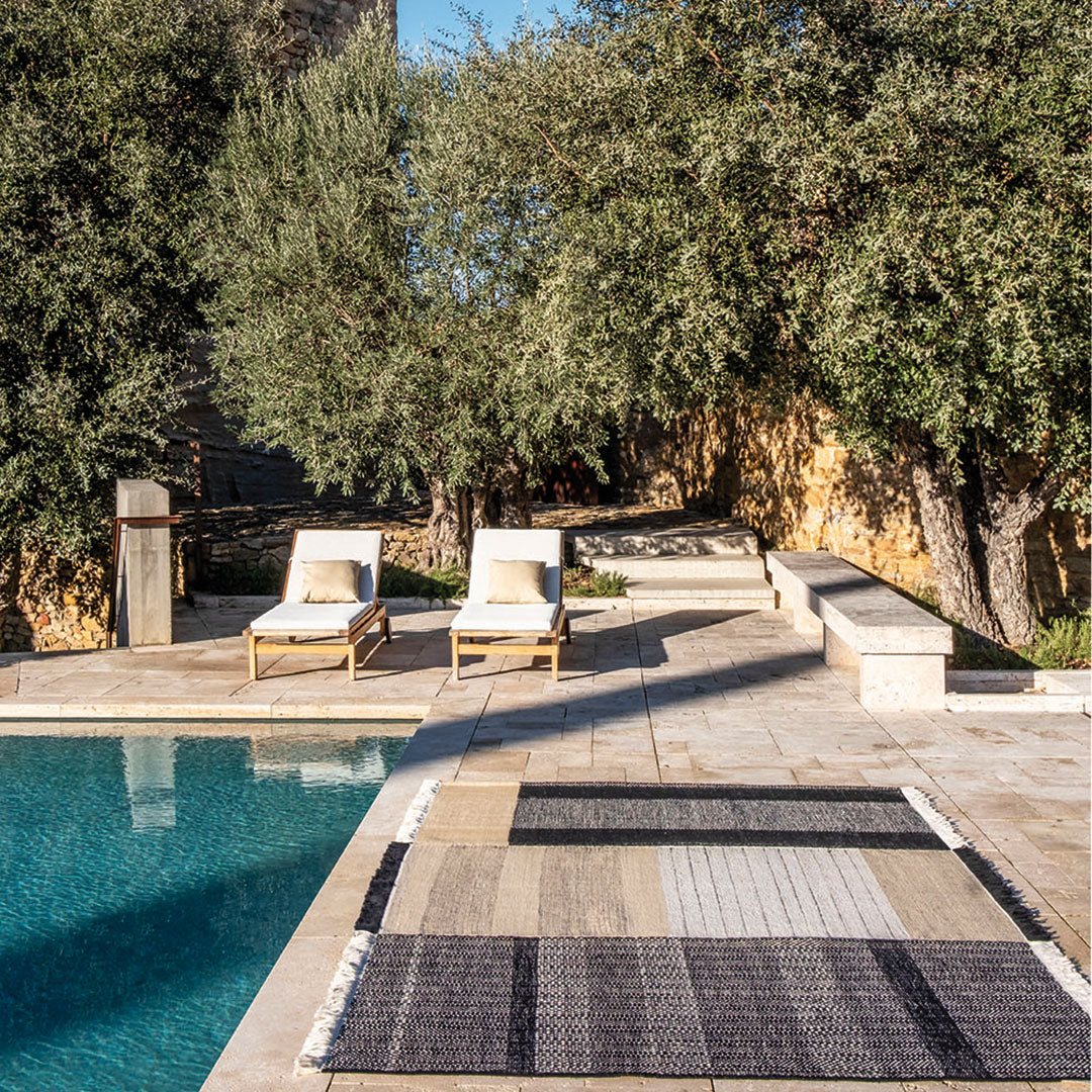 Rustic outdoor rug featuring shades of beige, gray, and textured patterns, perfect for poolside decor.