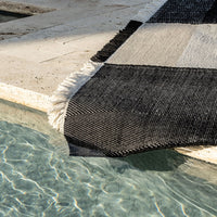 Black and white geometric patterned rug with fringed edges, partially submerged in clear water.