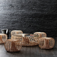 Woven rattan coffee table and stools in natural tones against a dark textured stone wall, showcasing elegant patterns.