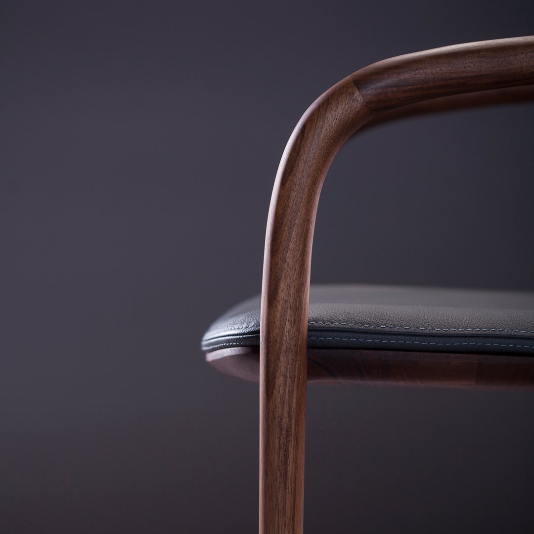 Elegant wooden chair with a sleek black seat against a dark backdrop, showcasing smooth curves and minimalist design.