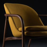 "Modern mustard yellow upholstered chair with curved design and wooden frame."