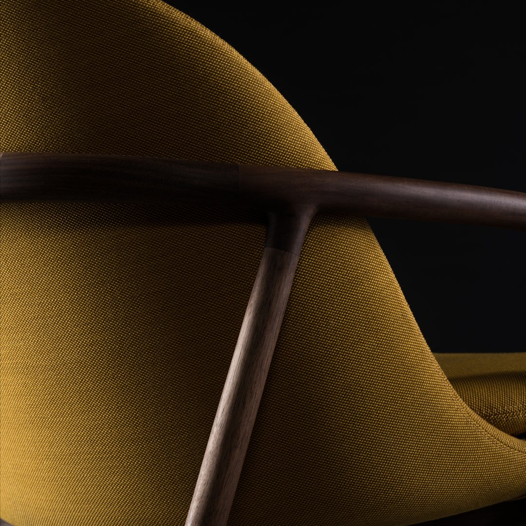 Curved mustard yellow upholstery with dark wood accents against a black background, highlighting modern design and texture.