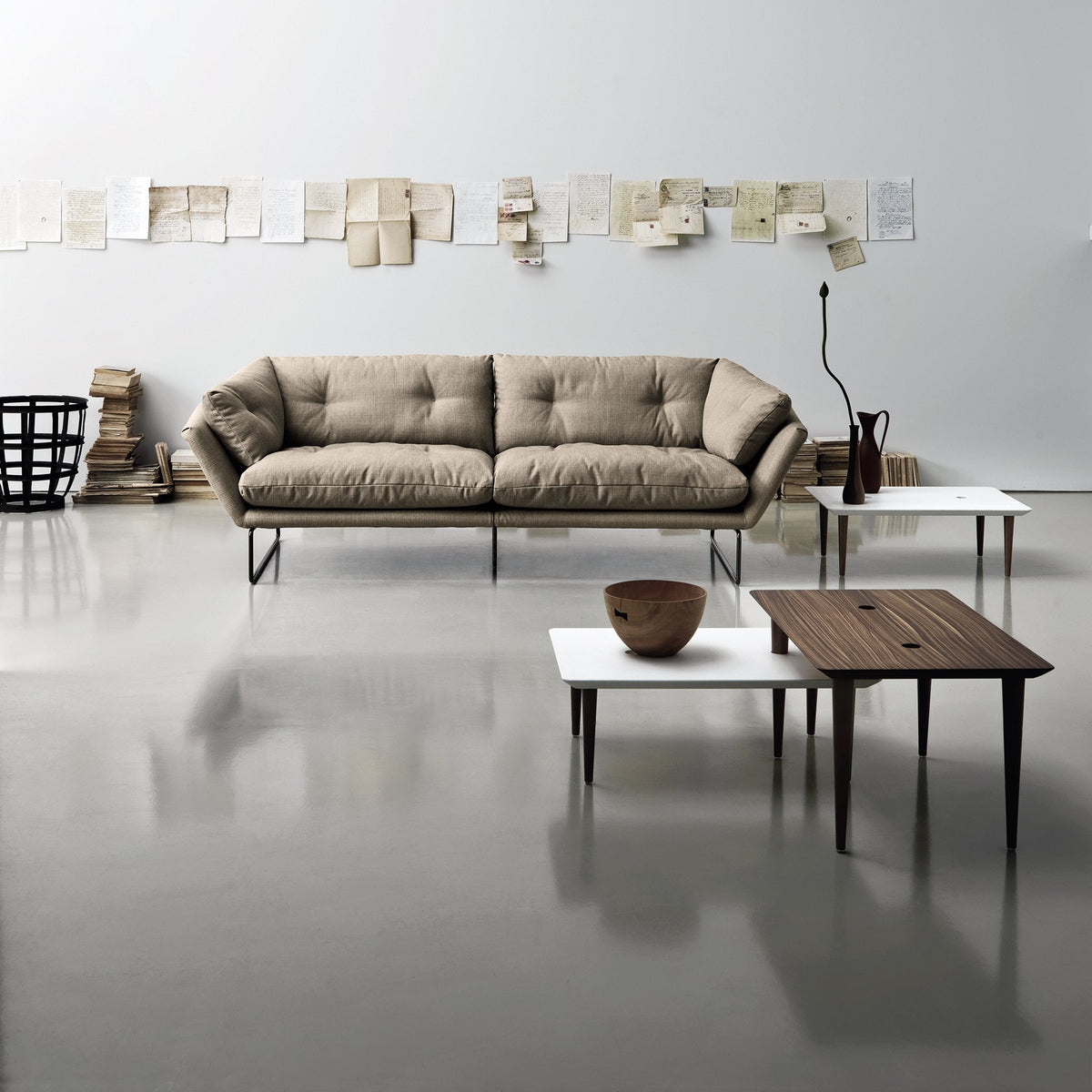 Beige tufted sofa with minimalist white and brown tables, set against a neutral wall and textured flooring.