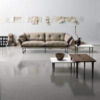 Beige tufted sofa with minimalist white and brown tables, set against a neutral wall and textured flooring.