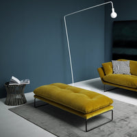 "Modern mustard yellow velvet ottoman with tufted design, paired with a gray rug and dark blue accent wall."