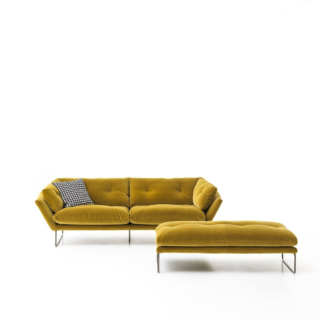 Yellow velvet sofa with a modern design, featuring a gray patterned throw pillow and sleek metal legs.