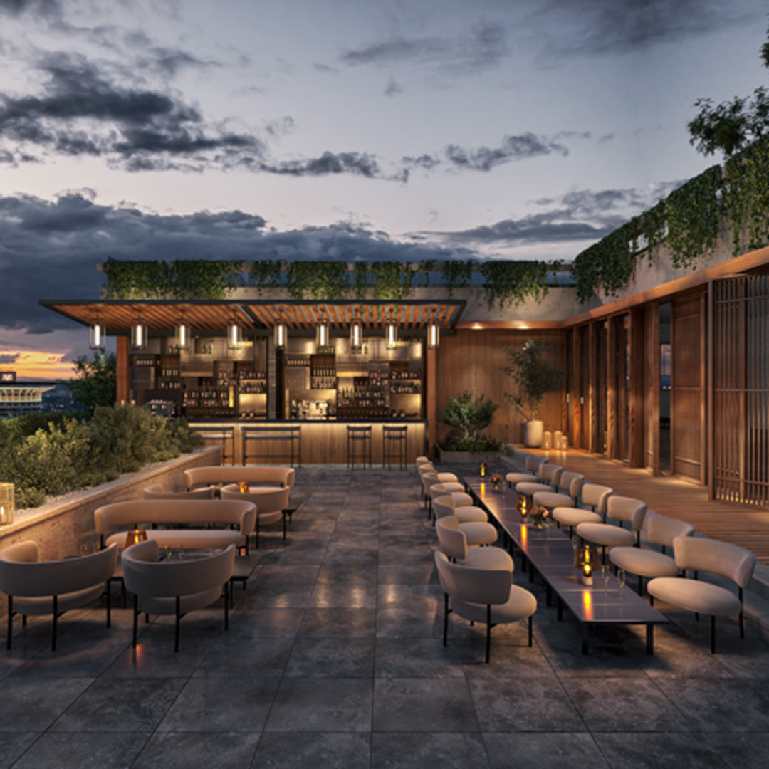 Stylish outdoor lounge with neutral beige furniture, green foliage, and warm wooden accents against a twilight sky.