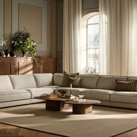 L-shaped light gray sofa with subtle texture and soft green accent pillows, paired with a round wooden coffee table.