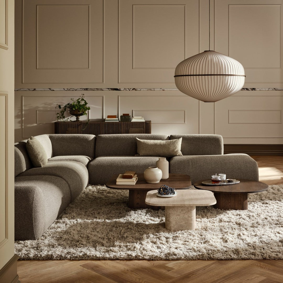 Gray sectional sofa with neutral, textured cushions, wooden tables, and a soft, shaggy rug in a warm, inviting room.