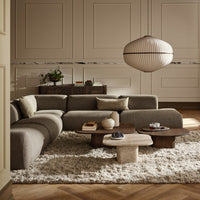 Gray sectional sofa with neutral, textured cushions, wooden tables, and a soft, shaggy rug in a warm, inviting room.