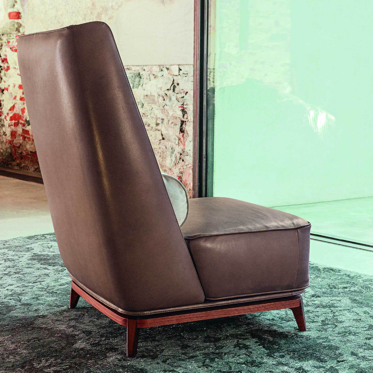 Brown leather accent chair with sleek design and wooden base, set against a textured green and patterned backdrop.