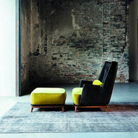 Black and yellow accent chair with a matching ottoman on a textured gray rug, against a rustic brick wall.