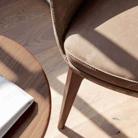 Brown suede chair with subtle stitching, complemented by a wooden table and natural sunlight casting soft shadows.