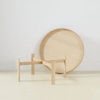 Natural wood finish with a smooth round tray and minimalist, angular leg design, showcasing warm tones and subtle grain patterns.